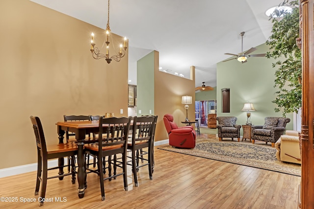 dining space with ceiling fan, light wood-style floors, a chandelier, baseboards, and high vaulted ceiling