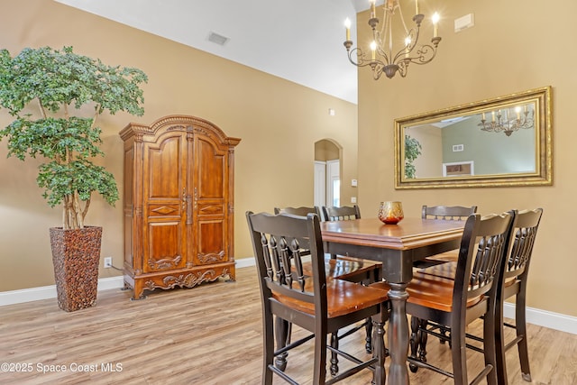 dining room featuring arched walkways, a chandelier, light wood finished floors, baseboards, and a towering ceiling