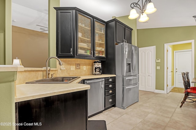 kitchen featuring stainless steel appliances, a sink, dark cabinetry, light countertops, and glass insert cabinets