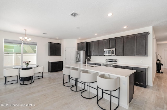 kitchen featuring appliances with stainless steel finishes, a sink, a kitchen breakfast bar, a chandelier, and light countertops