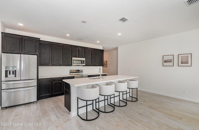 kitchen with appliances with stainless steel finishes, a sink, light wood-style floors, a kitchen breakfast bar, and a kitchen island with sink