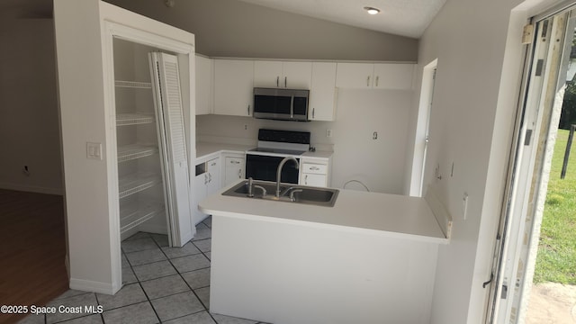 kitchen featuring stainless steel microwave, range with electric cooktop, a sink, lofted ceiling, and white cabinetry