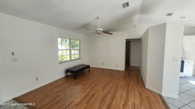 spare room featuring a ceiling fan, light wood-style flooring, a textured ceiling, vaulted ceiling, and baseboards