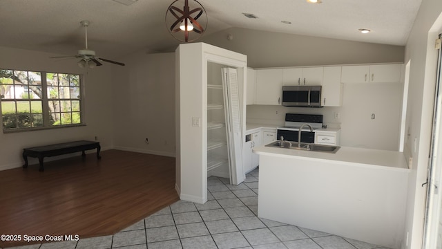 kitchen featuring stainless steel microwave, a sink, lofted ceiling, light countertops, and ceiling fan