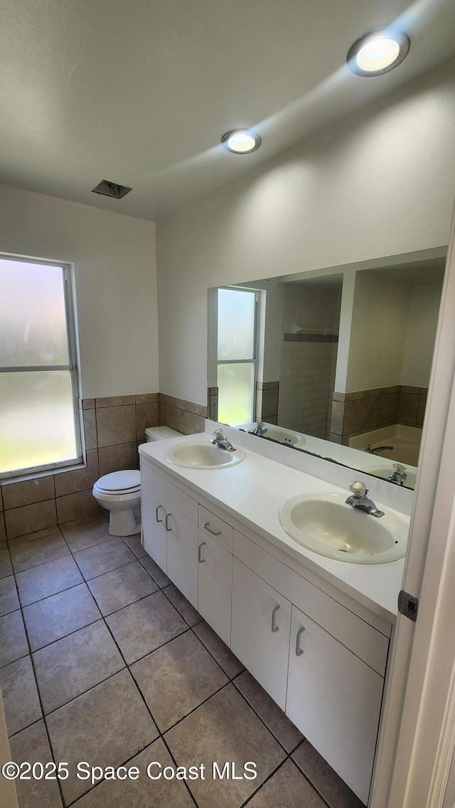 full bath with double vanity, tile patterned floors, a wainscoted wall, tile walls, and a shower