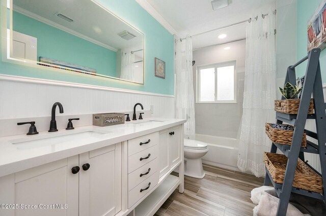 407 Sandpiper Dr, Satellite Beach, FL 32937 - bathroom featuring crown molding, toilet, double vanity, a wainscoted wall, and shower / bath combo