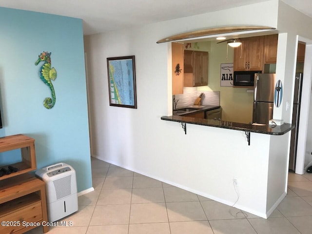 2625 S Atlantic Ave Unit 17, Cocoa Beach, FL 32931 - kitchen featuring black microwave, a kitchen bar, freestanding refrigerator, light tile patterned floors, and a peninsula
