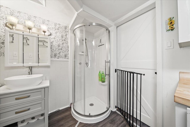 full bath featuring wood finished floors, a shower stall, vanity, a wainscoted wall, and wallpapered walls