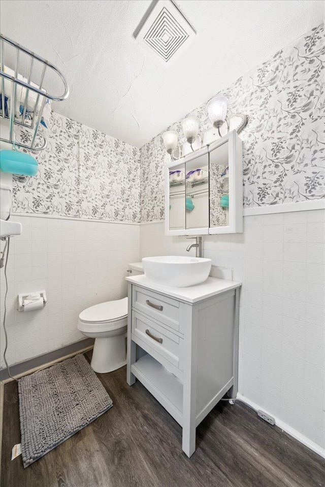 bathroom featuring a wainscoted wall, wallpapered walls, wood finished floors, tile walls, and toilet