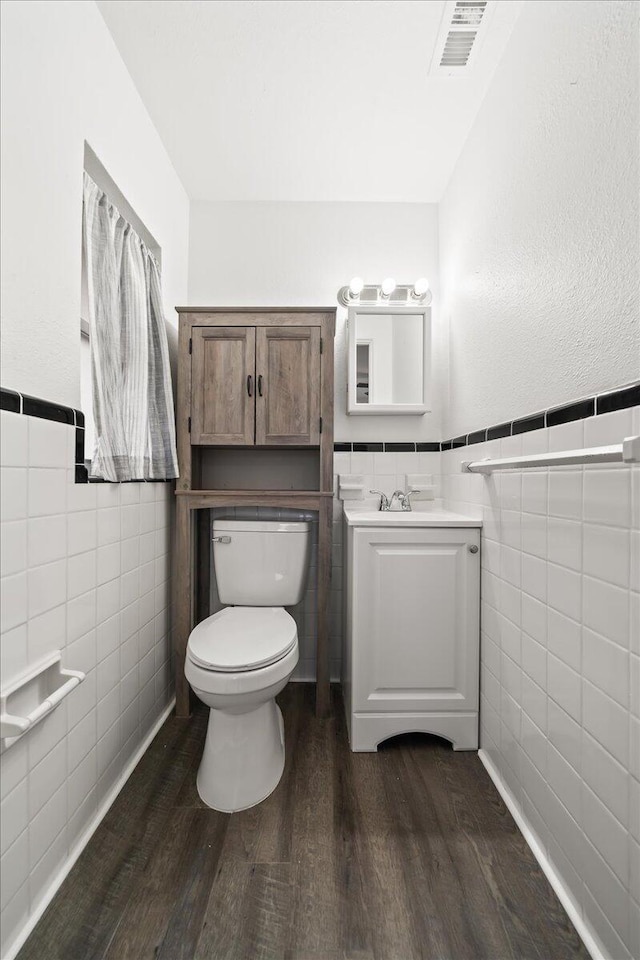 half bathroom with tile walls, wood finished floors, toilet, wainscoting, and vanity