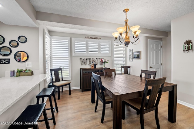 dining room featuring light wood-type flooring, a chandelier, a textured ceiling, and baseboards