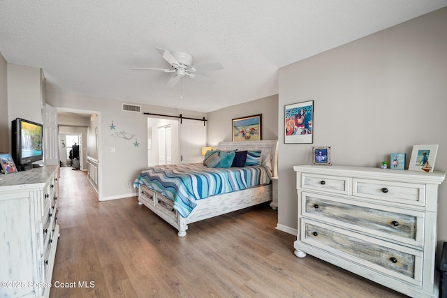 bedroom with wood finished floors, baseboards, a barn door, a textured ceiling, and ceiling fan