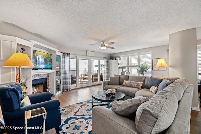 living room featuring ceiling fan, wood finished floors, a textured ceiling, and a tile fireplace
