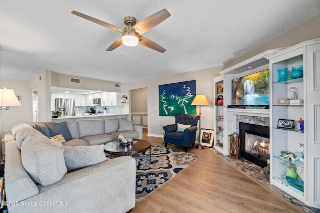 living room with a textured ceiling, a premium fireplace, a ceiling fan, and wood finished floors