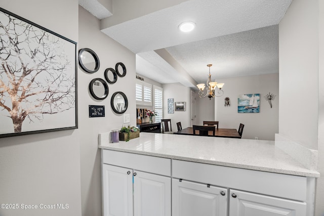 kitchen with a textured ceiling, white cabinets, a chandelier, pendant lighting, and light stone counters
