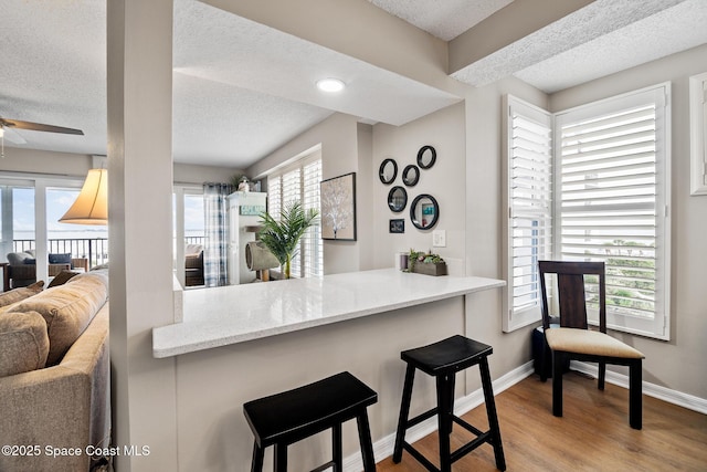 kitchen with a textured ceiling, wood finished floors, baseboards, a ceiling fan, and a kitchen bar