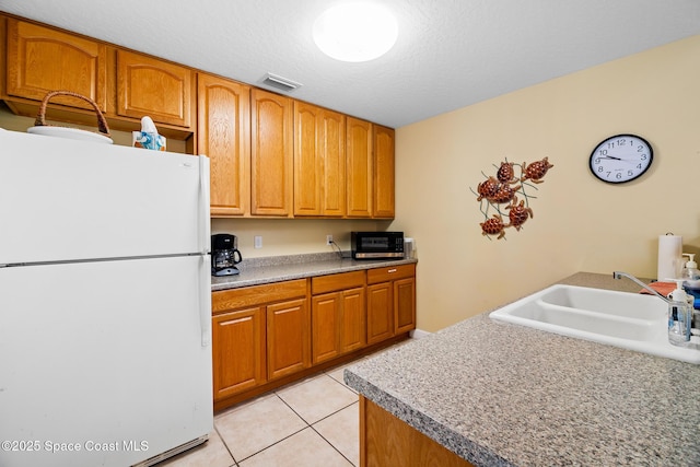 kitchen with freestanding refrigerator, a sink, light tile patterned flooring, brown cabinets, and a textured ceiling