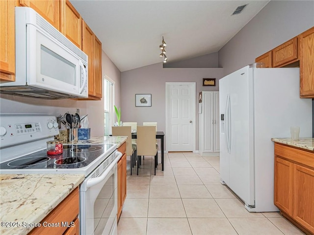 kitchen with white appliances, vaulted ceiling, light tile patterned flooring, light stone counters, and brown cabinets