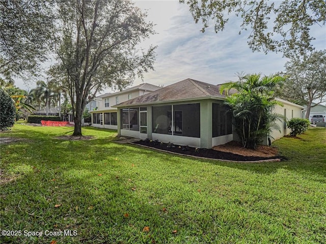 back of house featuring a sunroom, a lawn, stucco siding, and a shingled roof