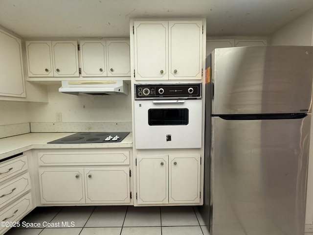 kitchen with freestanding refrigerator, oven, under cabinet range hood, black electric cooktop, and light countertops