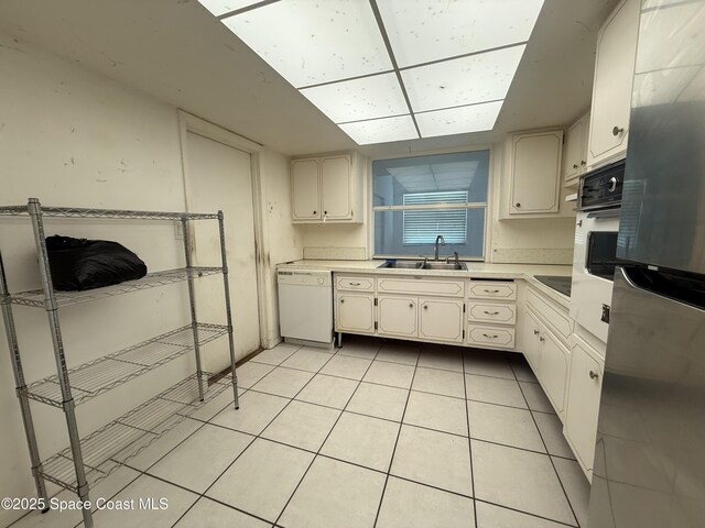 kitchen with a sink, white appliances, light tile patterned flooring, and light countertops