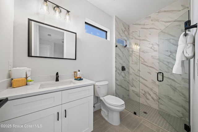 full bath with a marble finish shower, vanity, and toilet