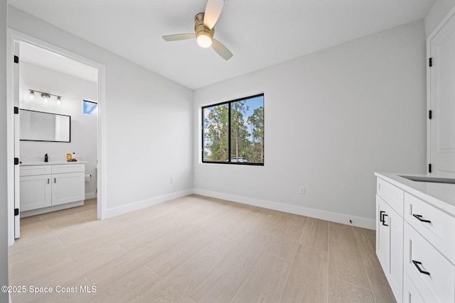 unfurnished bedroom with baseboards, light wood-style flooring, ensuite bath, a ceiling fan, and a sink