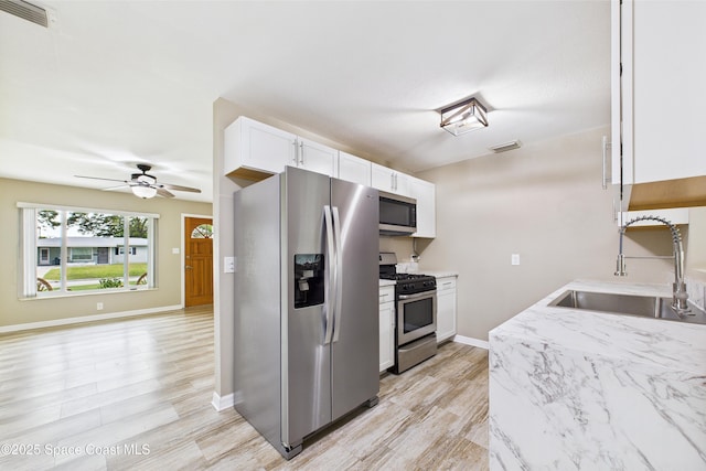 2341 Pawnee Dr, Melbourne, FL 32935 - kitchen with stainless steel appliances, a sink, white cabinets, ceiling fan, and light wood finished floors