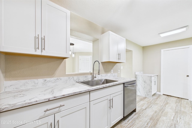 2341 Pawnee Dr, Melbourne, FL 32935 - kitchen with stainless steel dishwasher, a sink, white cabinetry, light stone counters, and light wood-style flooring