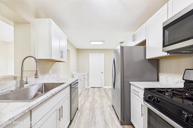 2341 Pawnee Dr, Melbourne, FL 32935 - kitchen featuring appliances with stainless steel finishes, a sink, light wood-style flooring, white cabinetry, and light stone countertops
