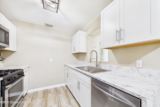 2341 Pawnee Dr, Melbourne, FL 32935 - kitchen featuring stainless steel appliances, a sink, white cabinetry, light stone countertops, and baseboards