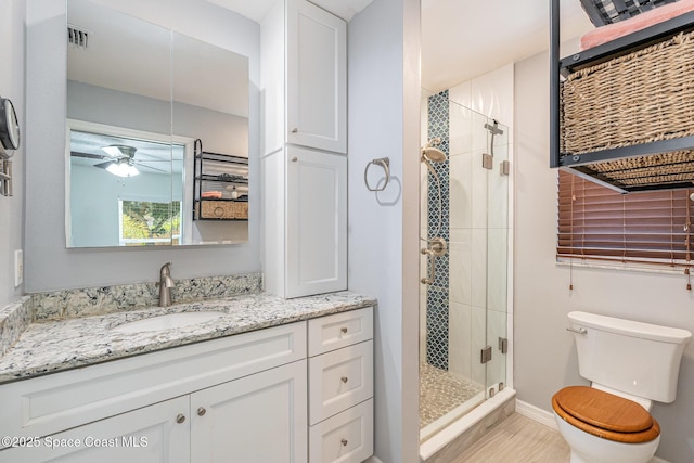 full bathroom featuring a stall shower, toilet, vanity, a ceiling fan, and baseboards