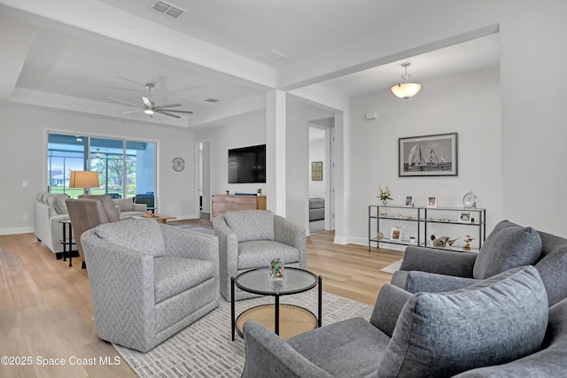 living area featuring light wood-style floors, baseboards, a ceiling fan, and a tray ceiling