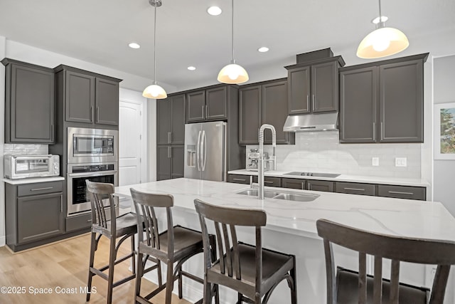 kitchen featuring appliances with stainless steel finishes, a sink, under cabinet range hood, tasteful backsplash, and pendant lighting