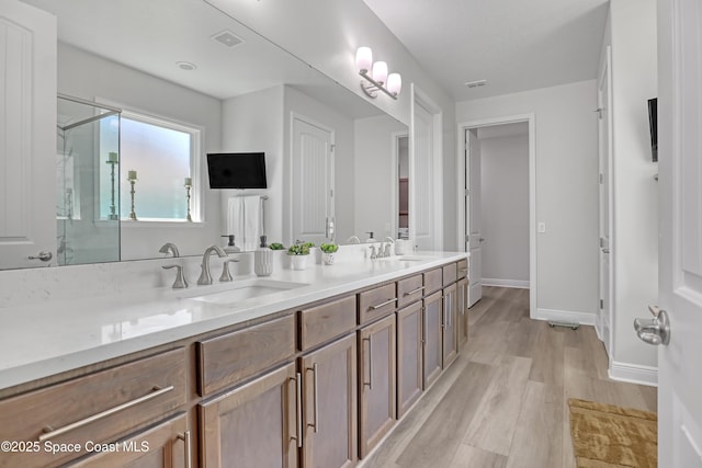 bathroom featuring wood finished floors, a shower stall, double vanity, and baseboards