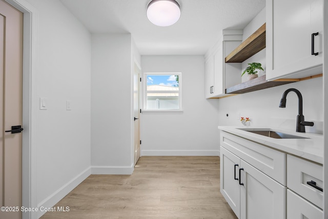bar featuring a sink, light wood finished floors, and baseboards