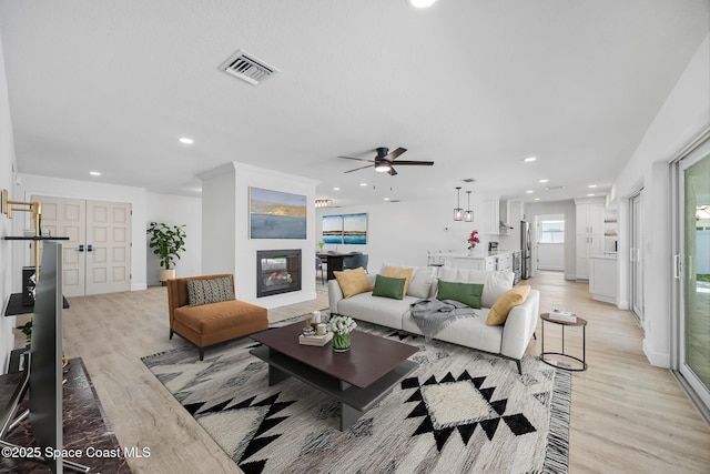 living area featuring light wood finished floors, a ceiling fan, recessed lighting, a glass covered fireplace, and baseboards