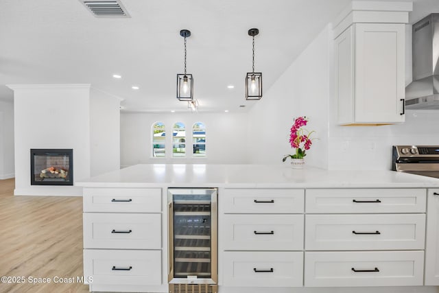 bar with wine cooler, electric range, wall chimney exhaust hood, light wood-type flooring, and hanging light fixtures