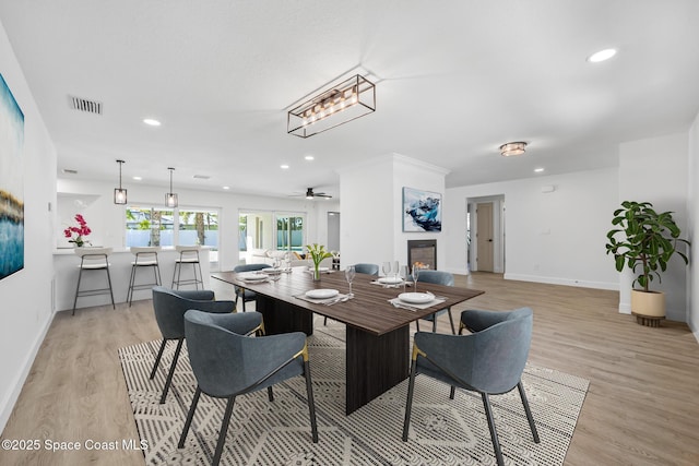 dining room featuring light wood finished floors, recessed lighting, baseboards, a lit fireplace, and a ceiling fan