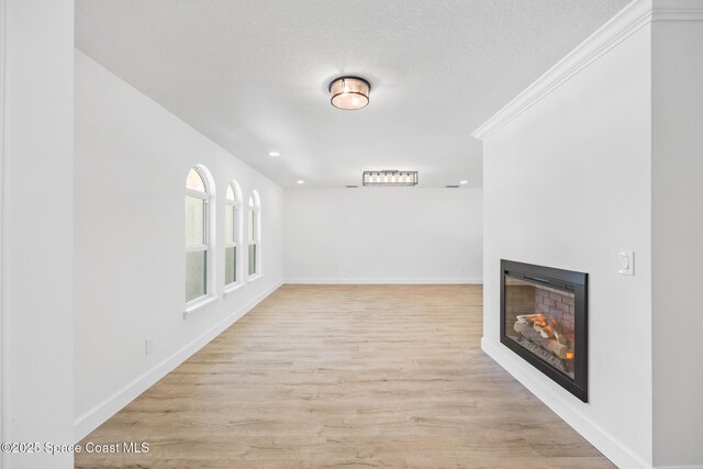 hall with light wood finished floors, baseboards, a textured ceiling, and recessed lighting