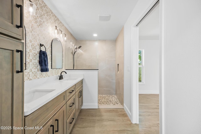 bathroom with a walk in shower, wood finished floors, double vanity, and baseboards