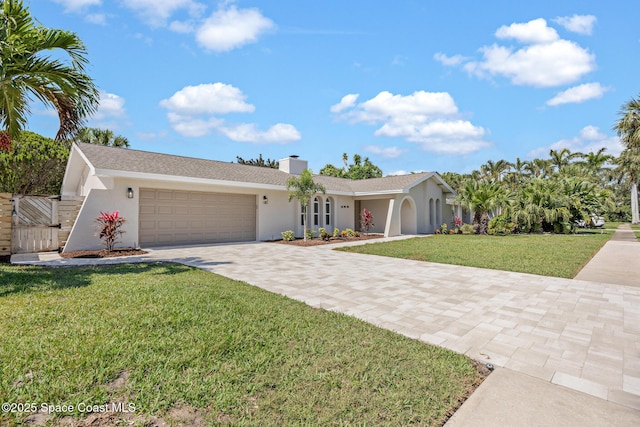 ranch-style house featuring driveway, an attached garage, a chimney, a front lawn, and stucco siding
