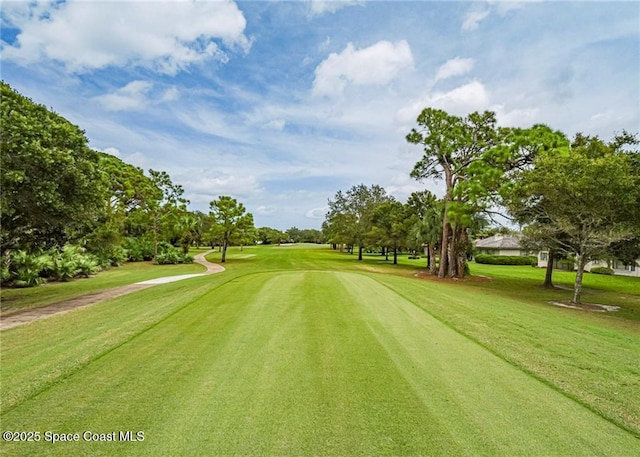view of property's community with golf course view, a lawn, and view of wooded area