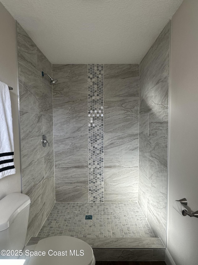 bathroom with toilet, tiled shower, and a textured ceiling