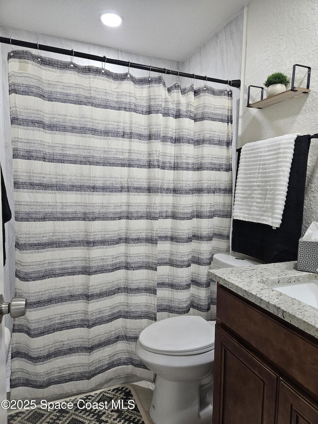 bathroom with a textured wall, toilet, vanity, and curtained shower