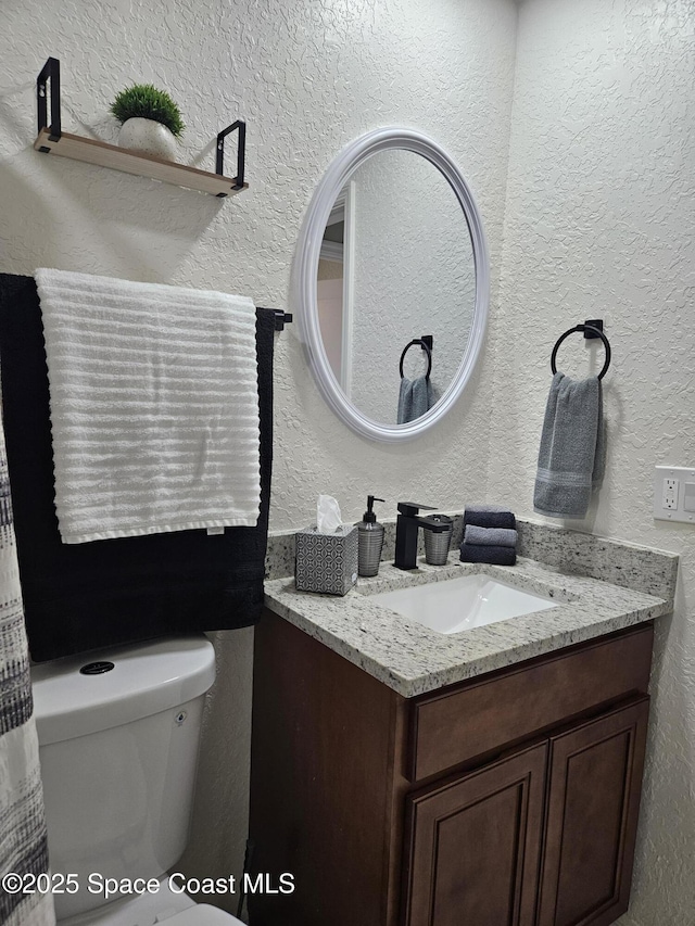 bathroom with a textured wall, toilet, and vanity