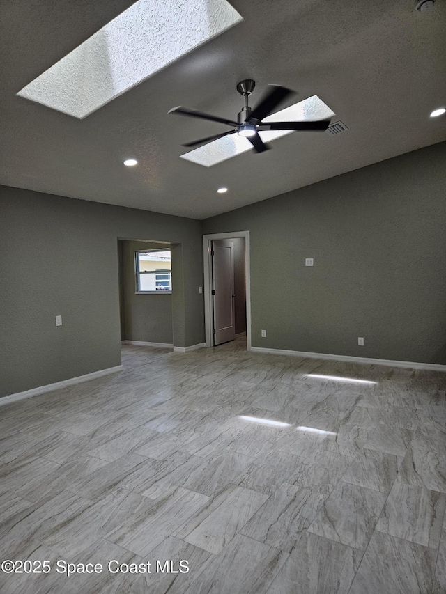 empty room featuring a skylight, a ceiling fan, baseboards, and recessed lighting