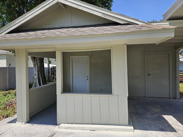 entrance to property with a shingled roof and fence