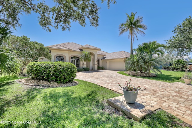 mediterranean / spanish home featuring stucco siding, an attached garage, a front lawn, decorative driveway, and a tiled roof