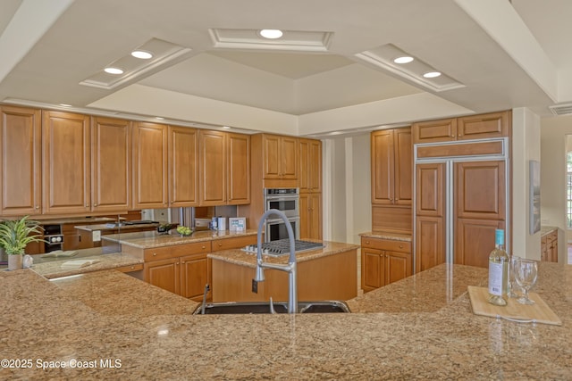 kitchen with paneled built in refrigerator, a sink, light stone countertops, recessed lighting, and double oven